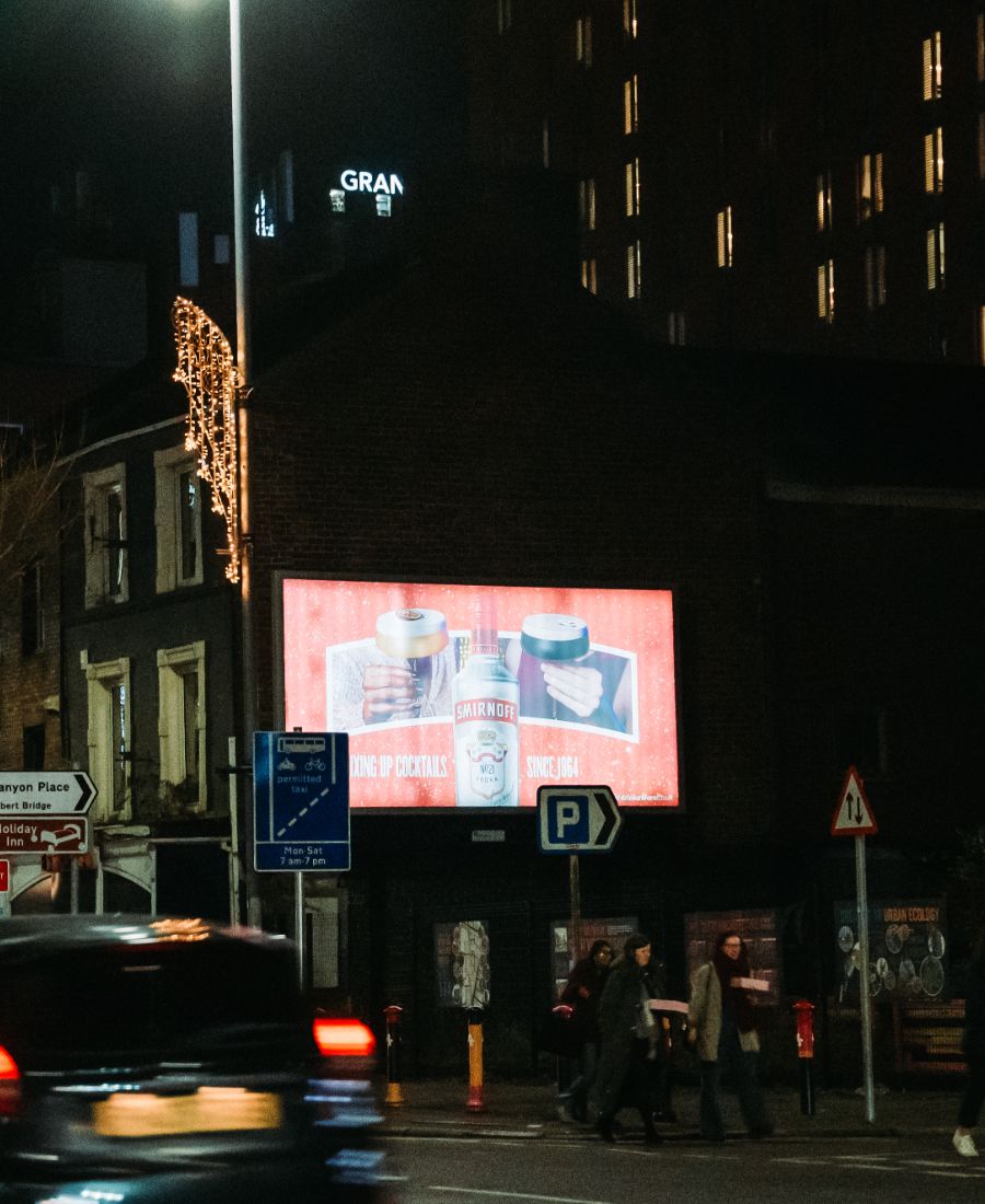 People walking by smirnoff ice ad at night